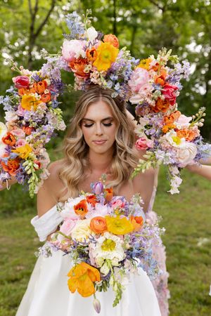 A wedding scene with vibrant floral arch and bouquet featuring orange, yellow, pink and purple blooms in a garden setting.