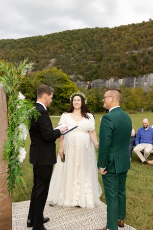 Outdoor wedding ceremony with couple and officiant against mountain backdrop.