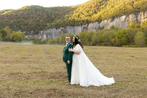 Couple in wedding attire pose against scenic mountain landscape.