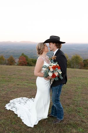 A couple shares a romantic kiss on a hilltop during their rustic country wedding with a scenic mountain backdrop.