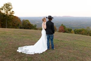 A couple stands together on a hilltop overlooking mountains during sunset with fall foliage in the background.