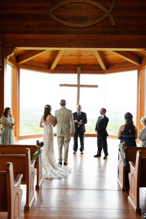 A wedding ceremony takes place in a wooden chapel with large windows overlooking scenic mountain views.