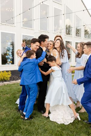 Wedding party members in blue and white outfits playfully pose together on a grassy lawn.