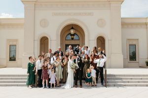 A large wedding party poses for a group photo on the steps of a white temple building.