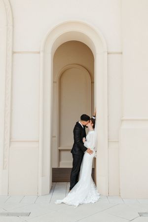 A couple embraces in an elegant arched doorway of a white stone building.