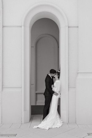 Black and white photo of couple in wedding attire sharing intimate moment in arched doorway.