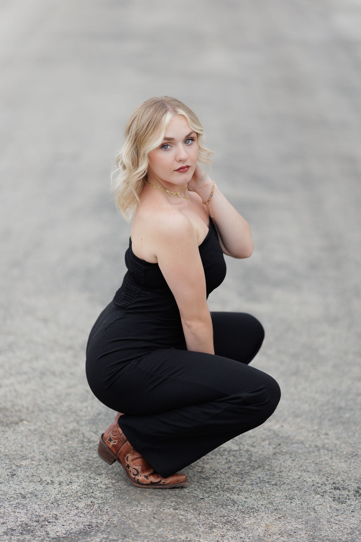 Blonde high school senior poses wearing cowgirl boots and black one piece.