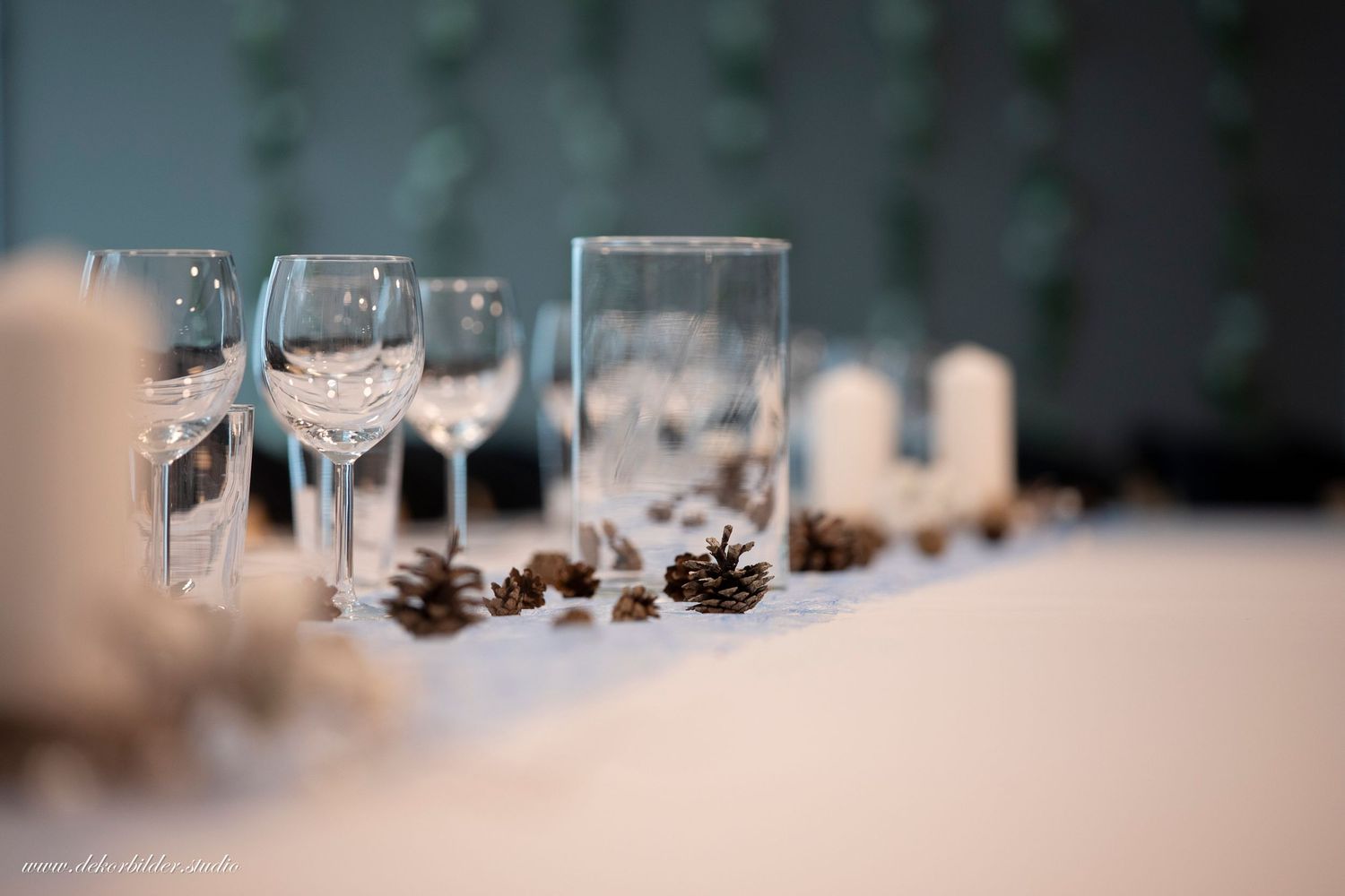Elegant table setting with wine glasses, candles, and pine cones at an event.