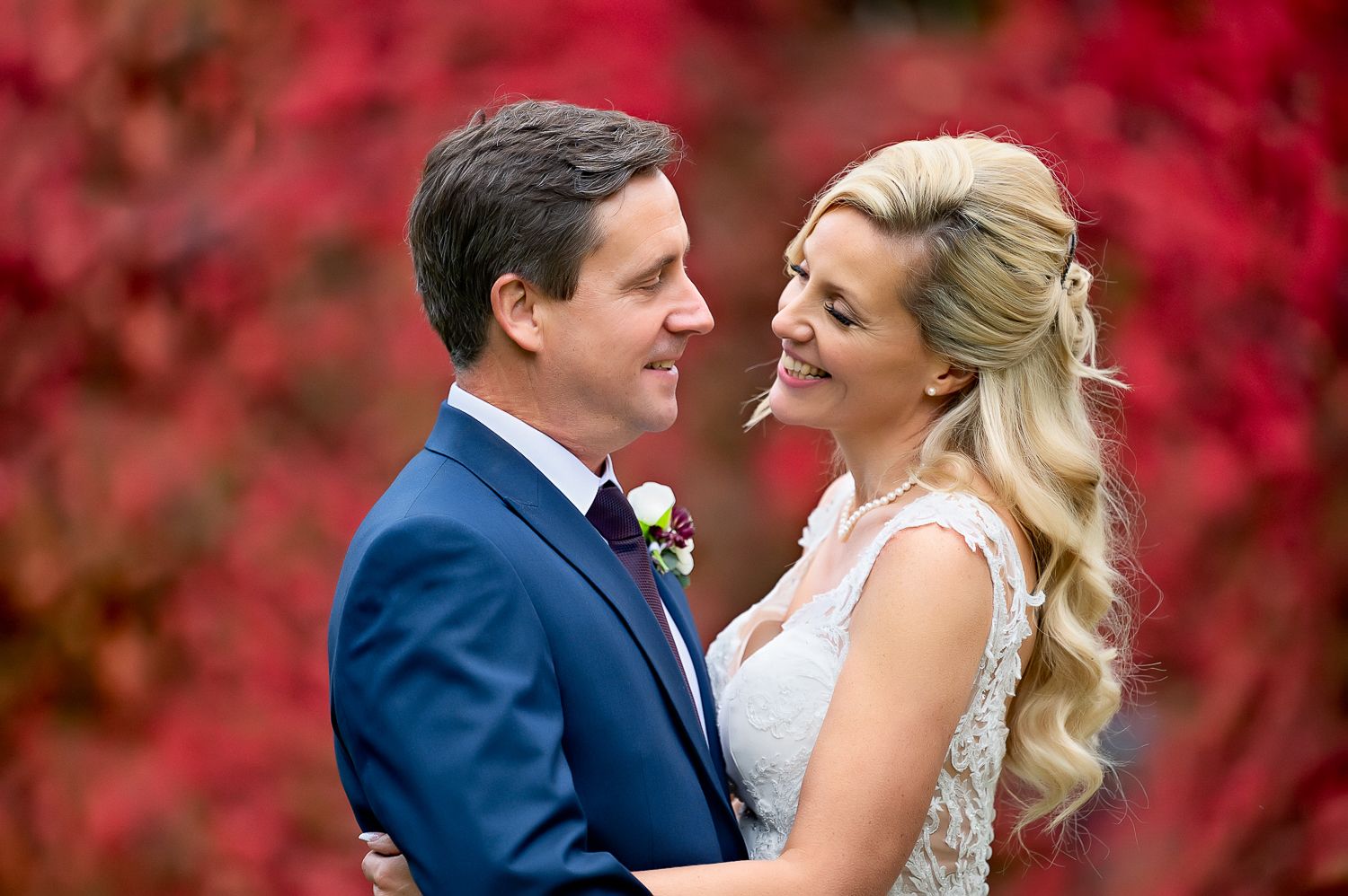 A wedding couple shares a loving moment against vibrant red autumn foliage.