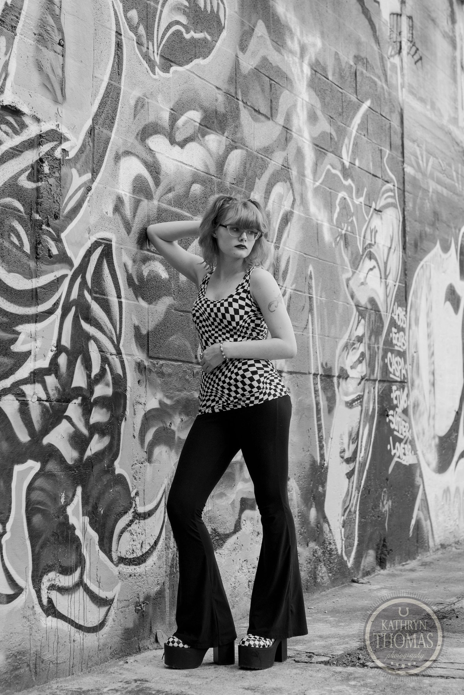 Black and white fashion photograph featuring geometric patterns against textured graffiti wall.