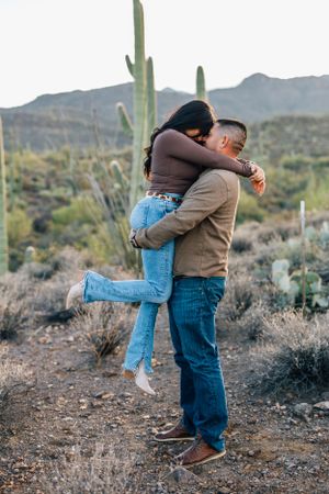 Tucson couples photography featuring a joyful hug and lift in the desert surrounded by saguaros and mountain views.