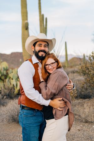 Tucson couples portrait of a man and woman hugging in the desert with tall saguaros and mountain scenery.