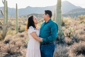 Romantic Tucson couples photo of a couple smiling at each other in the desert surrounded by saguaros and soft golden light.