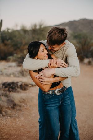 Warm Tucson couple portrait on a desert trail with mountains behind them.