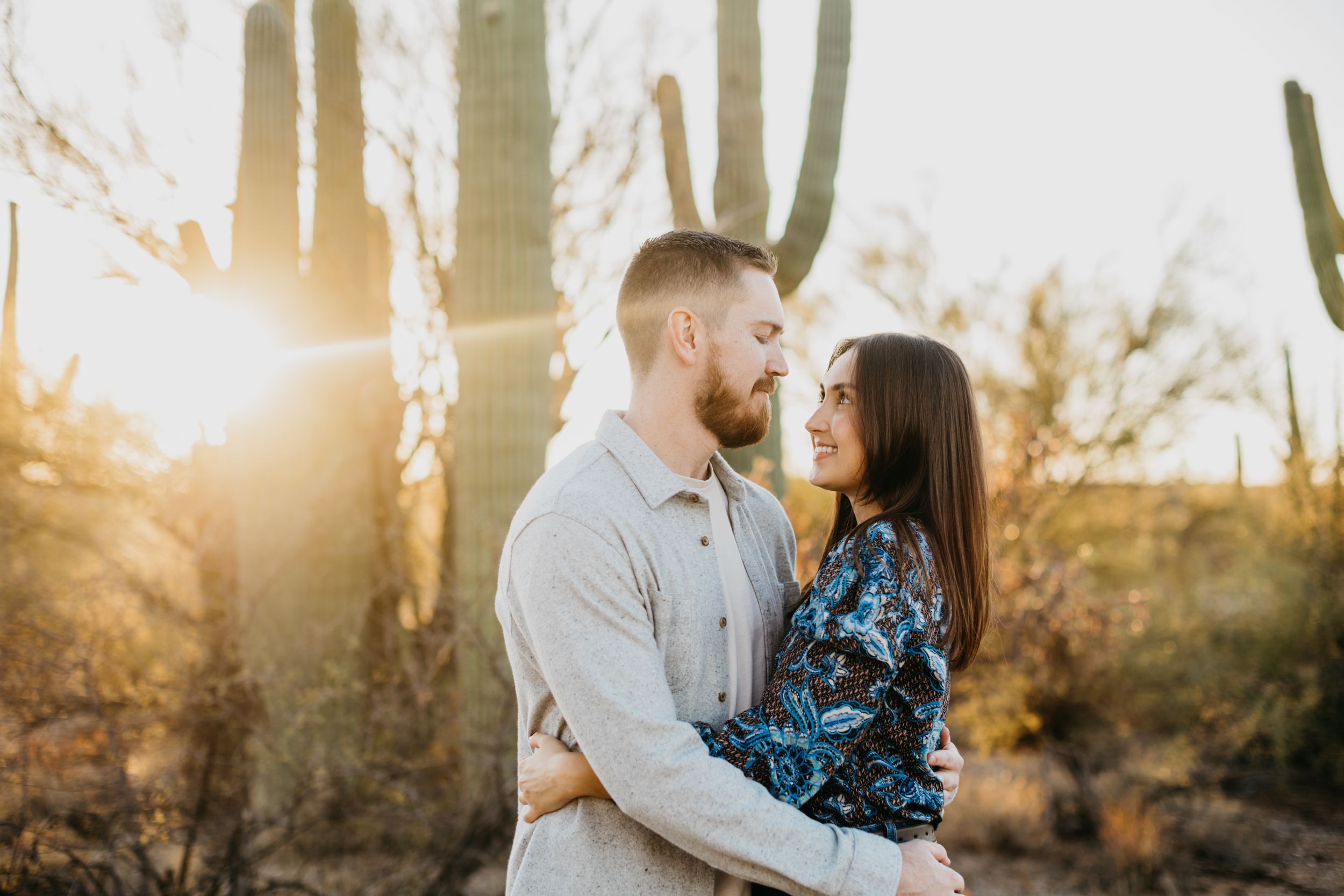 Tucson couples photo of a man and woman embracing at sunset with golden desert light streaming through the trees.