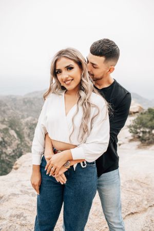 Tucson engagement photo of a couple standing on a rocky cliff in Mt. Lemmon with scenic desert mountain views.