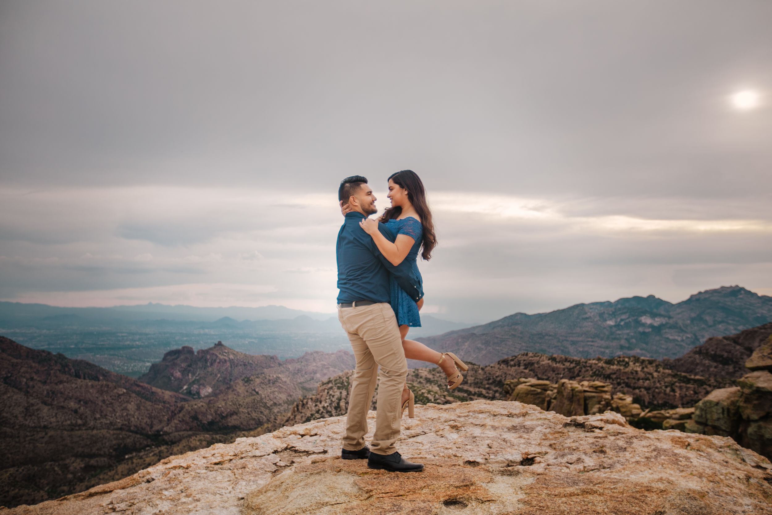 Romantic Tucson engagement photo of a couple embracing in Mt. Lemmon with a dramatic sunset sky.