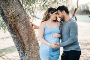 Tucson maternity photography of a couple embracing near a tree while holding the baby bump with warm natural lighting.