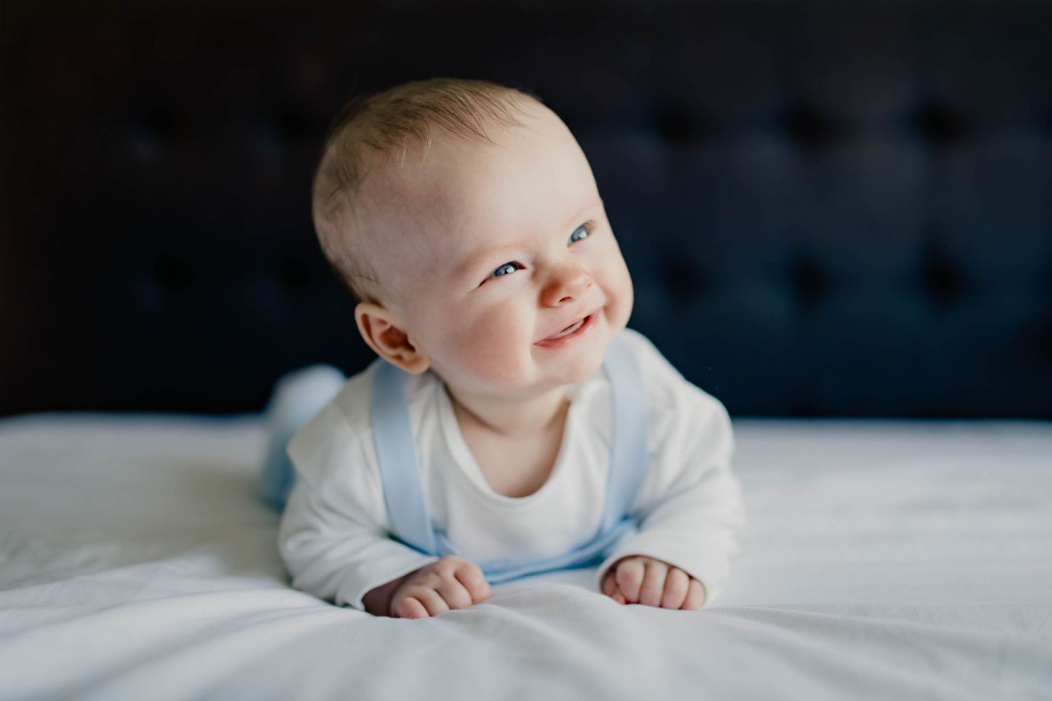 A smiling newborn baby boy crawls on a white bed