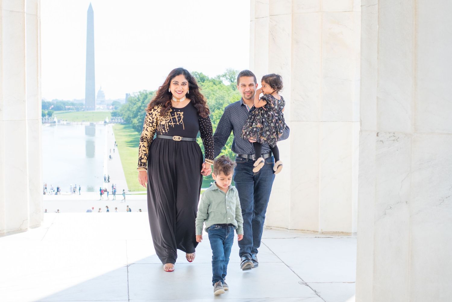 family of four walks in the Lincoln Memorial, Washington Monument and US Capitol behind them