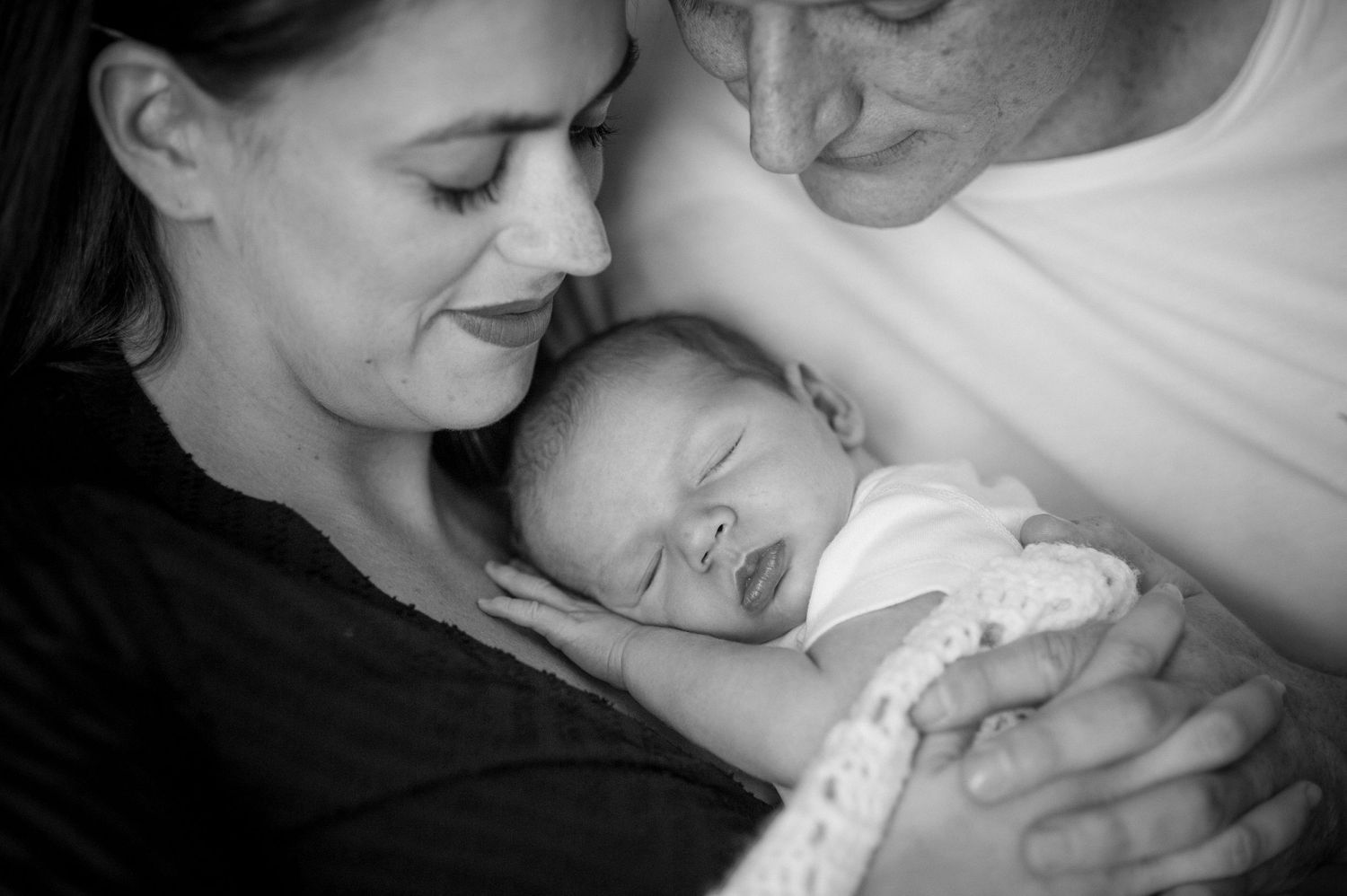 A tender black and white image of a sleeping newborn being cradled by loving parents.