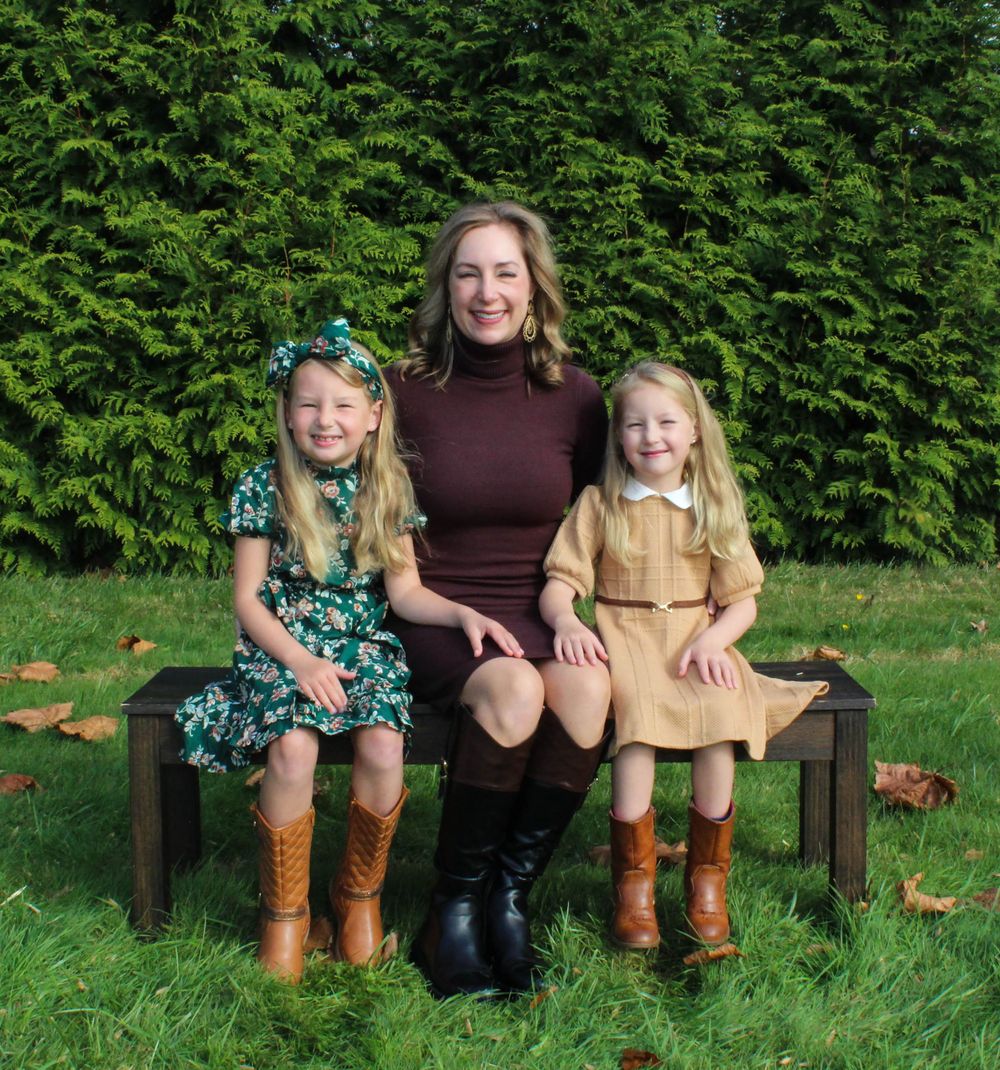 Three people sitting on wooden bench against hedge wearing coordinated brown and burgundy outfits.