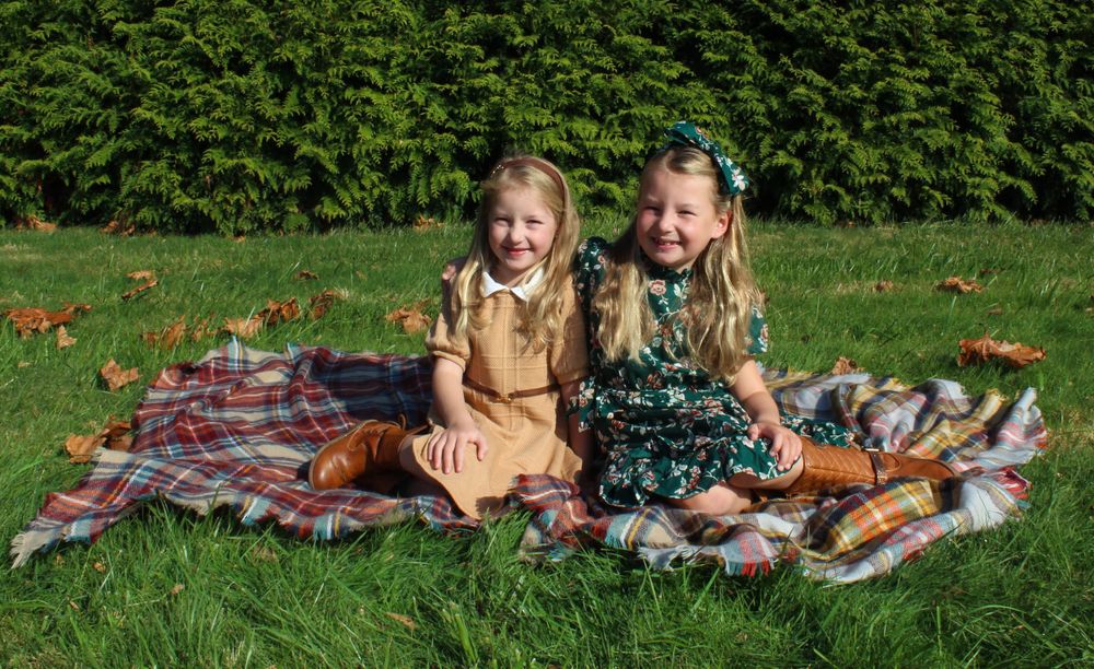 Two children in coordinating outfits pose on plaid blanket during outdoor photo session.