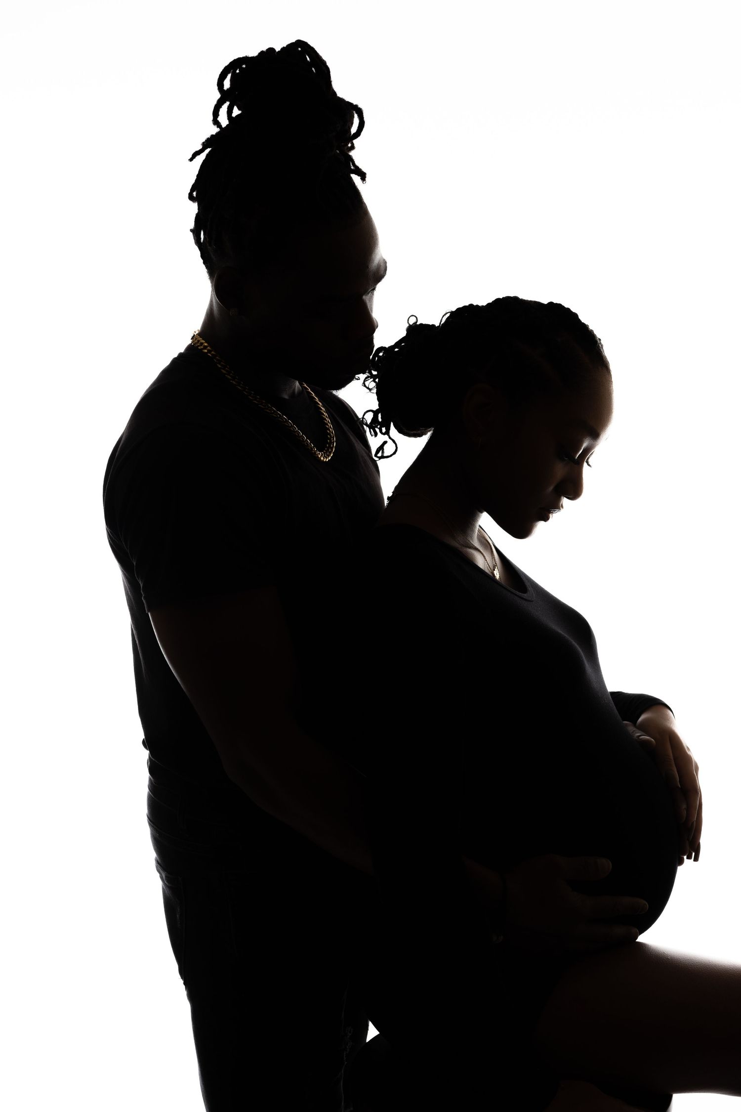 Silhouetted couple embraces in intimate maternity photoshoot against white background.