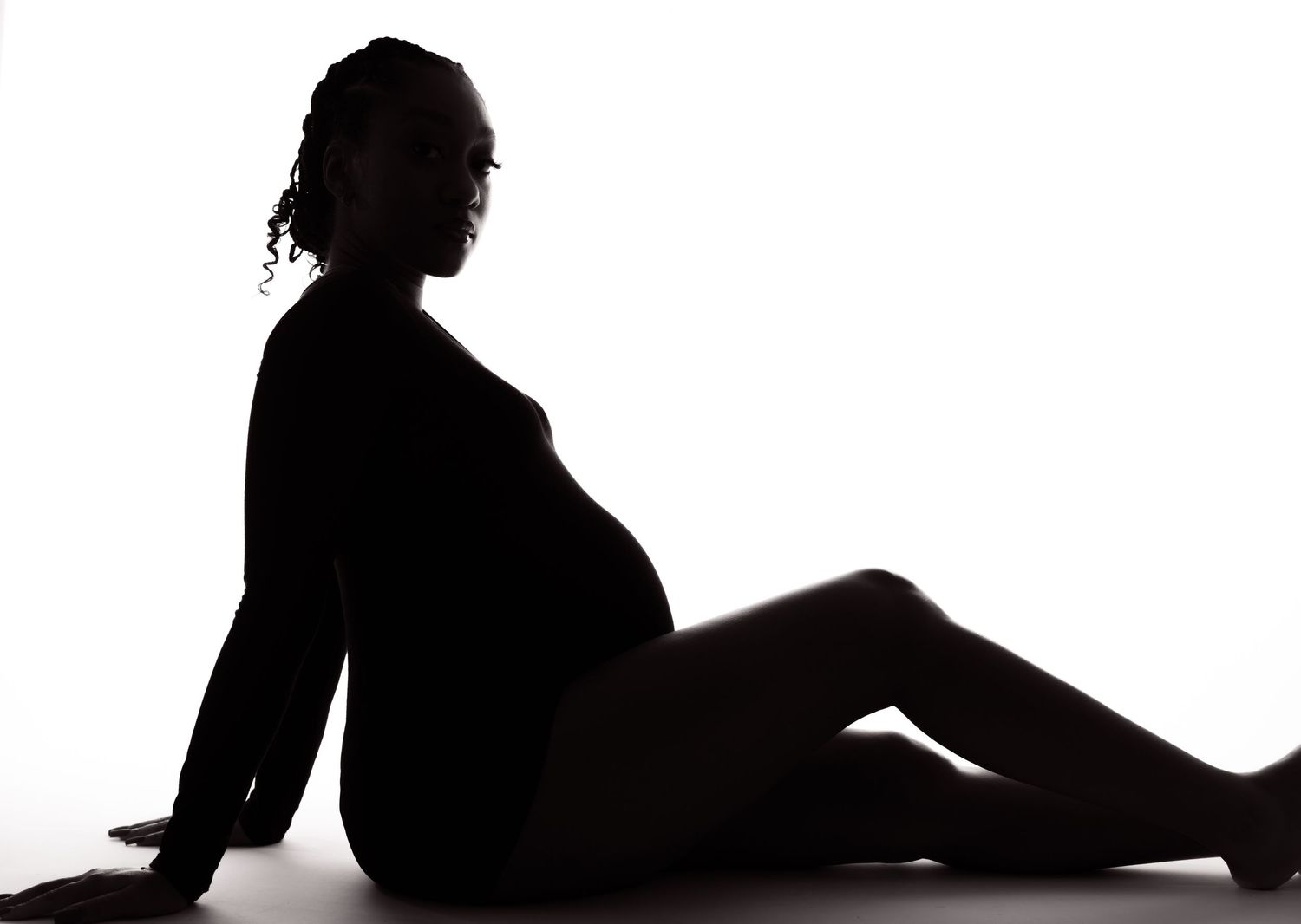 Artistic silhouette of pregnant woman reclining in profile against white background.