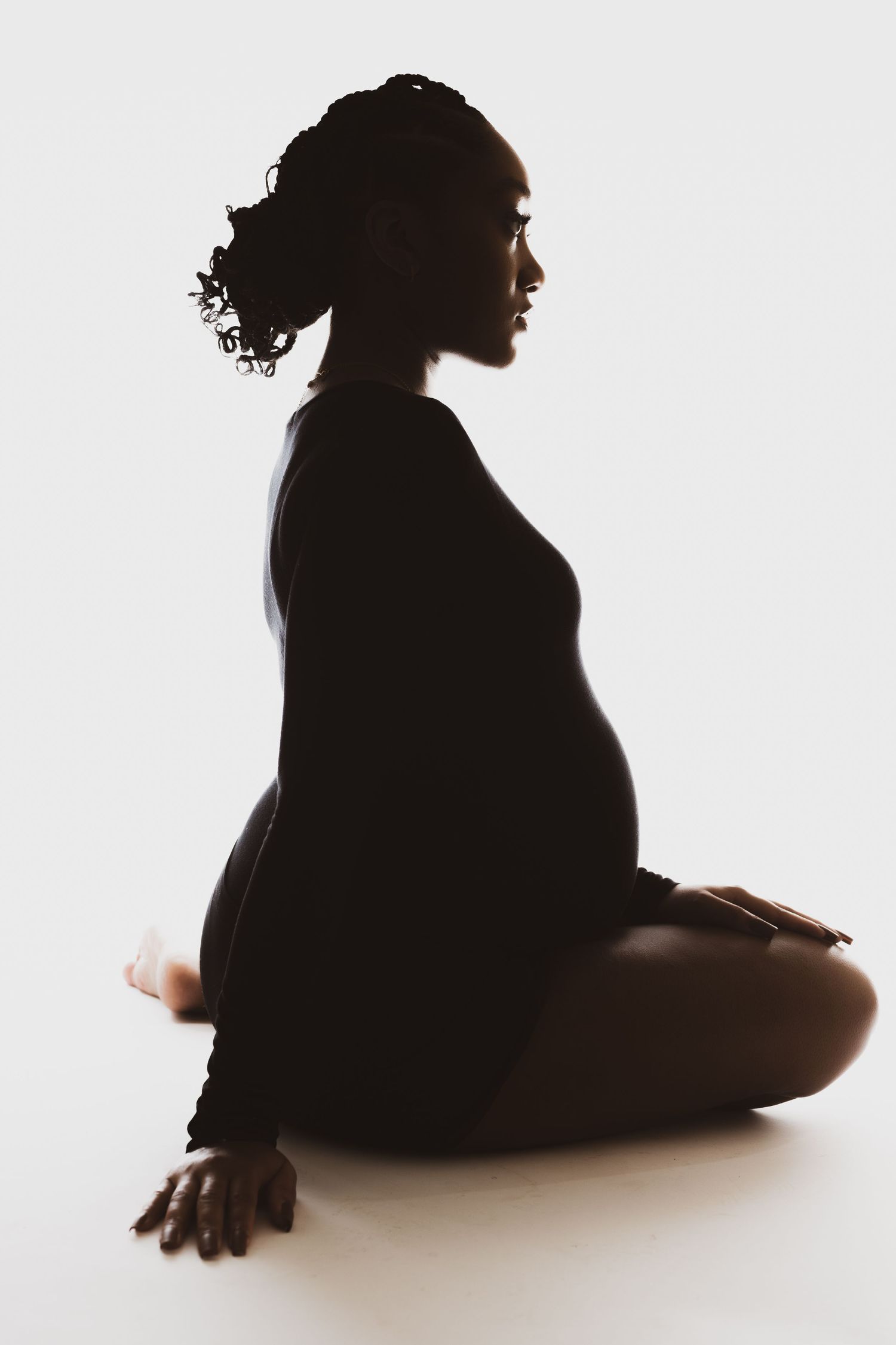 Side profile silhouette of pregnant woman sitting in elegant pose.