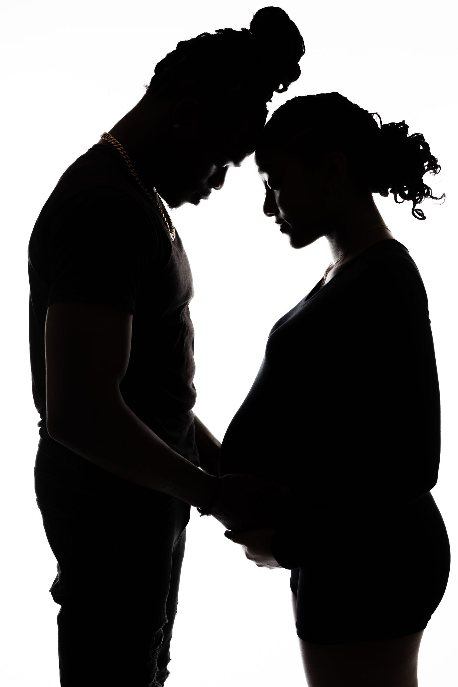 Silhouette portrait of expectant parents sharing tender moment against white backdrop.