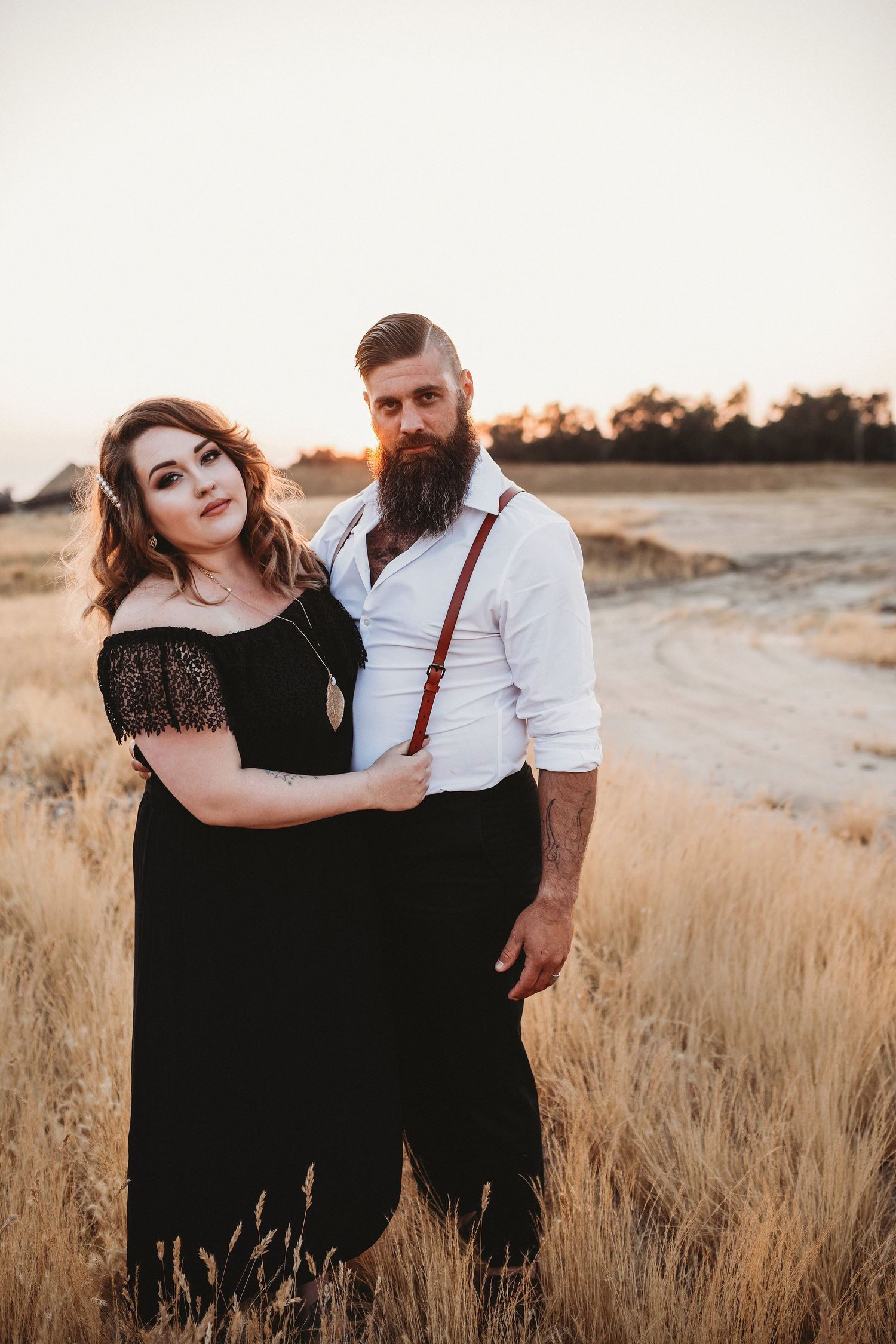 Couple in formal attire poses in golden field at sunset.