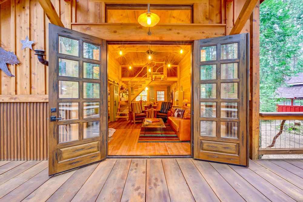 Rustic wooden cabin entrance with French doors opening to warmly lit interior space.
