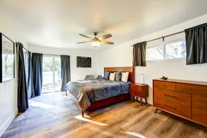Spacious master bedroom with wood flooring, ceiling fan, and dark curtains framing sliding doors.