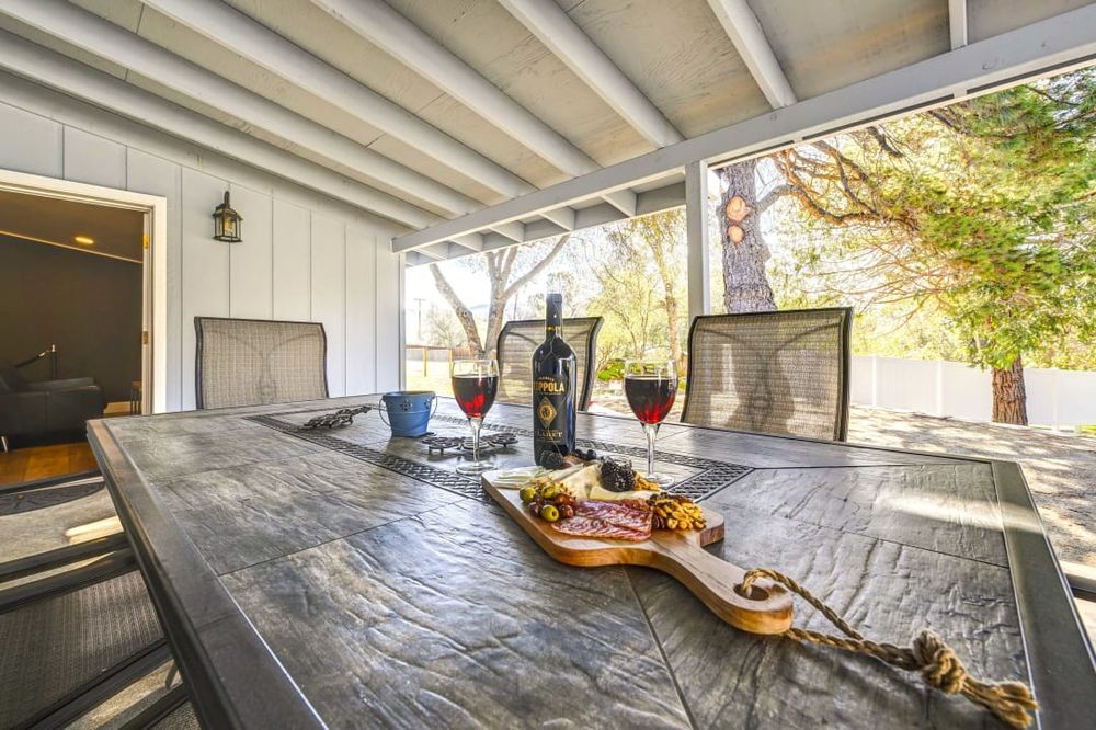 Covered outdoor patio with rustic wooden dining table and modern chairs overlooking garden.