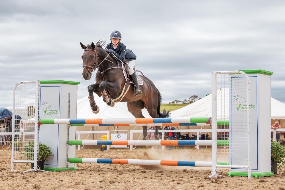 Horse and rider clearing jump obstacle during equestrian competition.