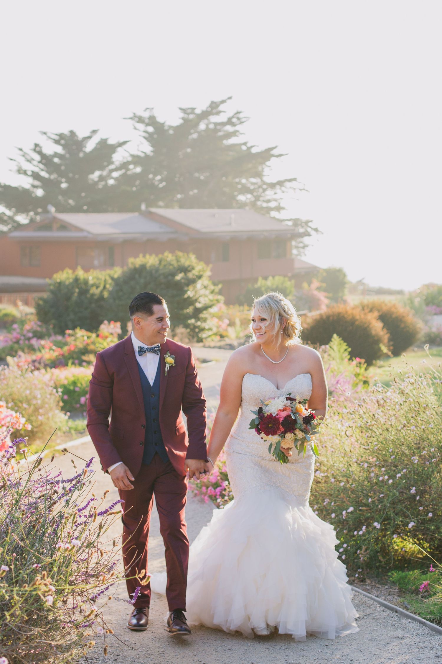 Couple walking through a garden path surrounded by blooming flowers at golden hour.