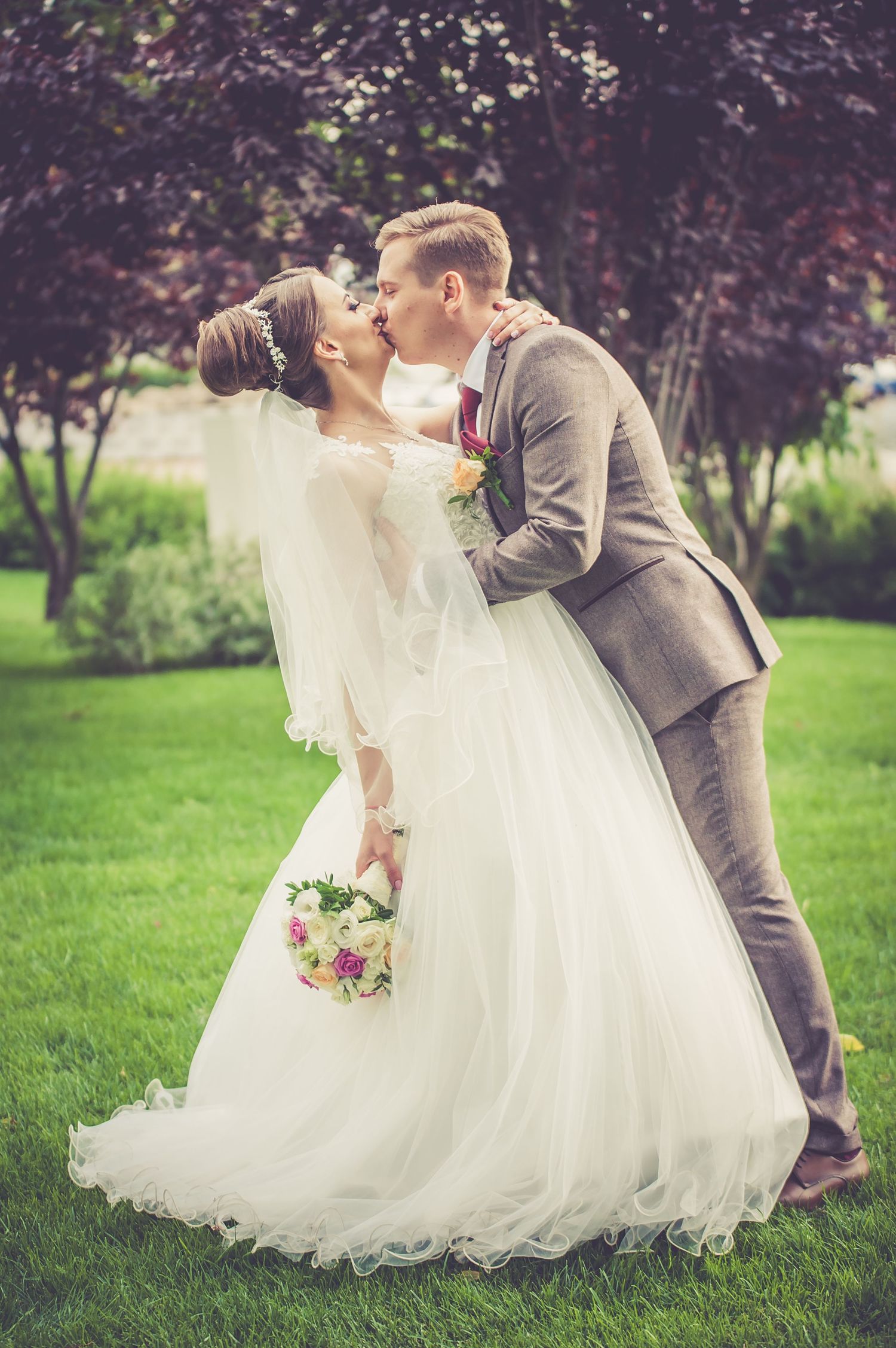 Romantic wedding portrait of couple embracing on garden lawn with vintage style editing.