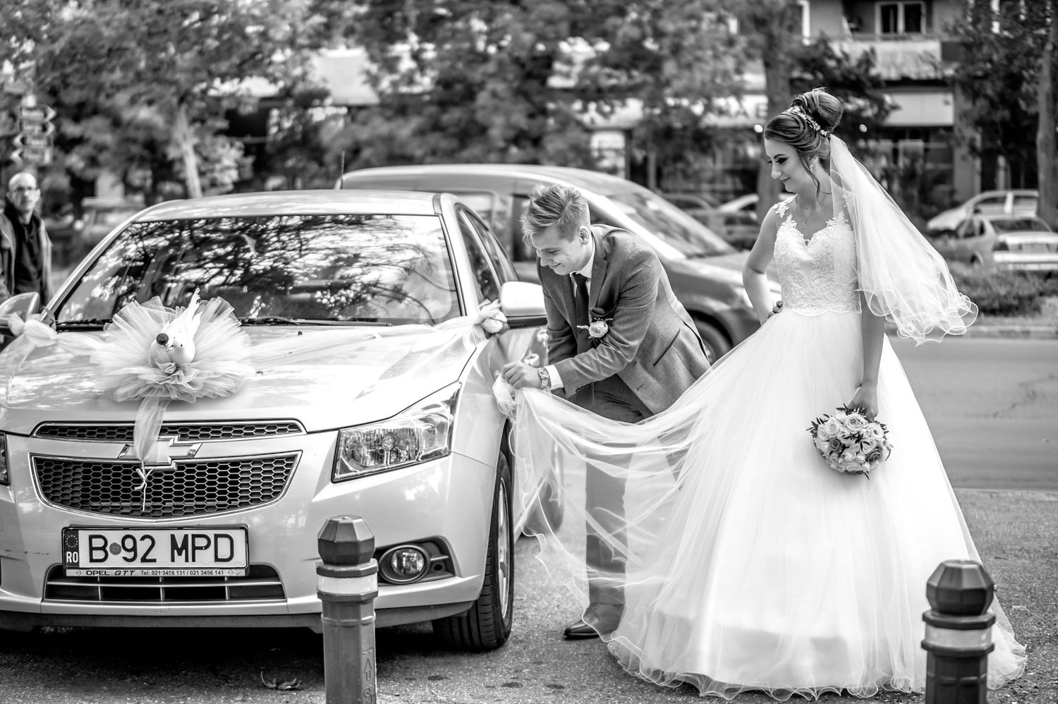 Wedding party gathered around a decorated Chevrolet car helping with the bride's dress.
