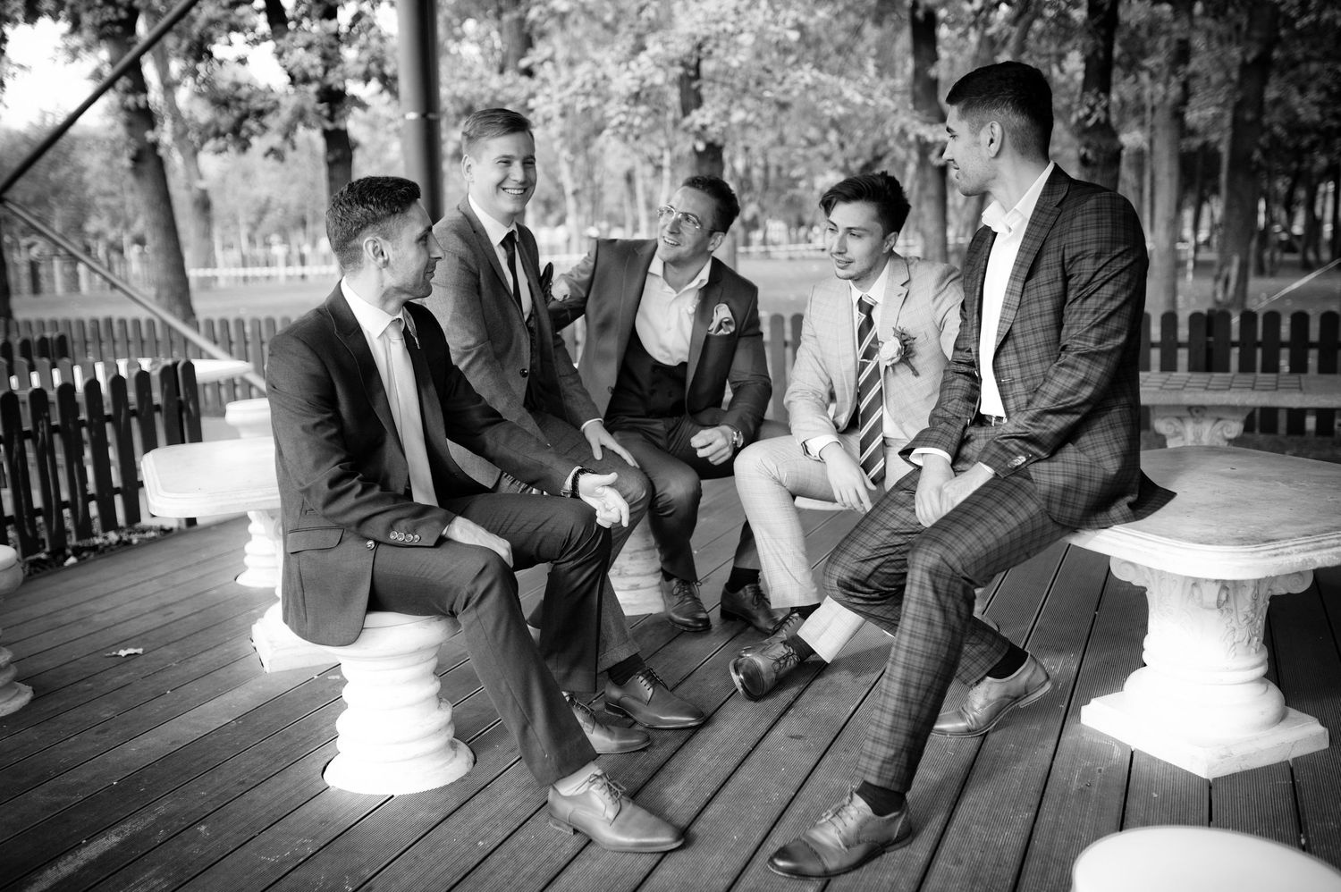 Black and white photo of wedding party relaxing on wooden deck outdoors.