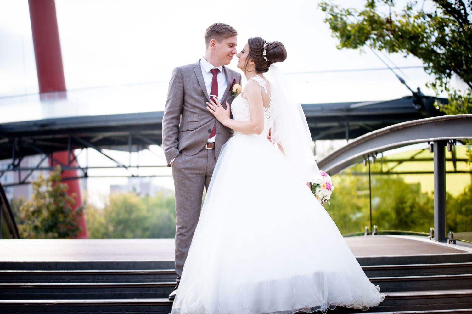 Elegant wedding couple poses on outdoor steps with urban backdrop.
