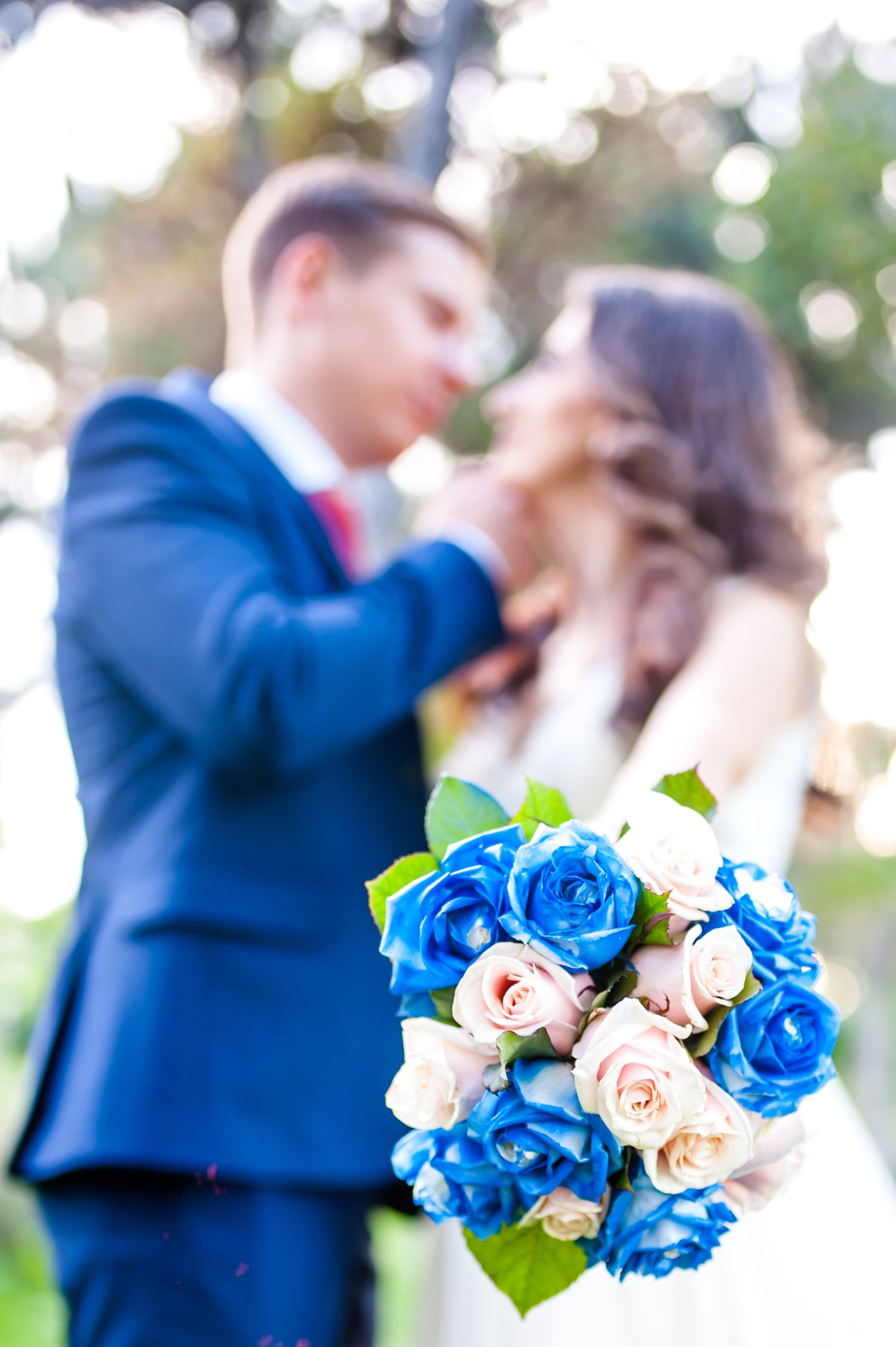Wedding bouquet with blue and white roses in focus with blurred couple in background.