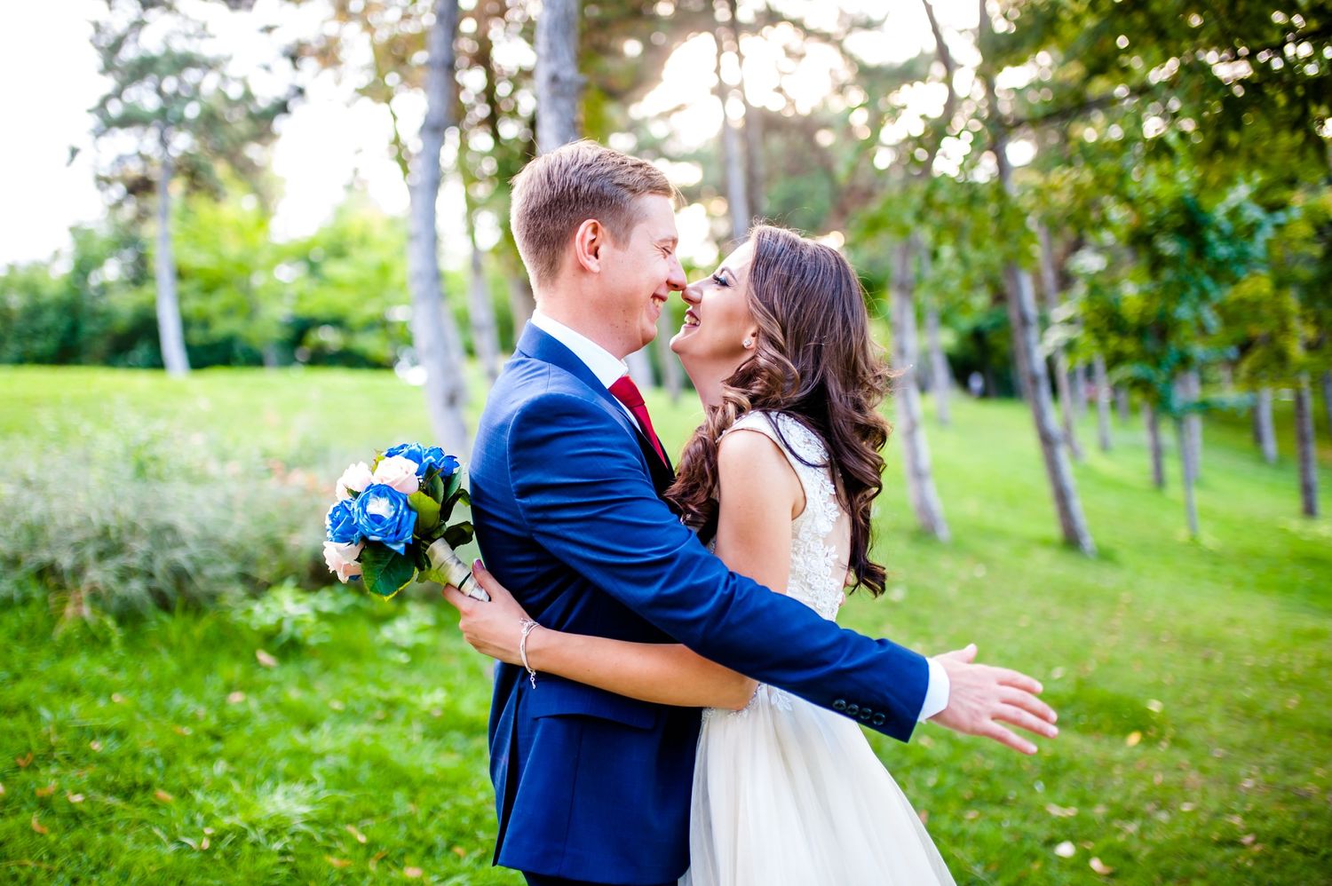 A romantic wedding couple embraces outdoors with blue flowers in a garden setting.