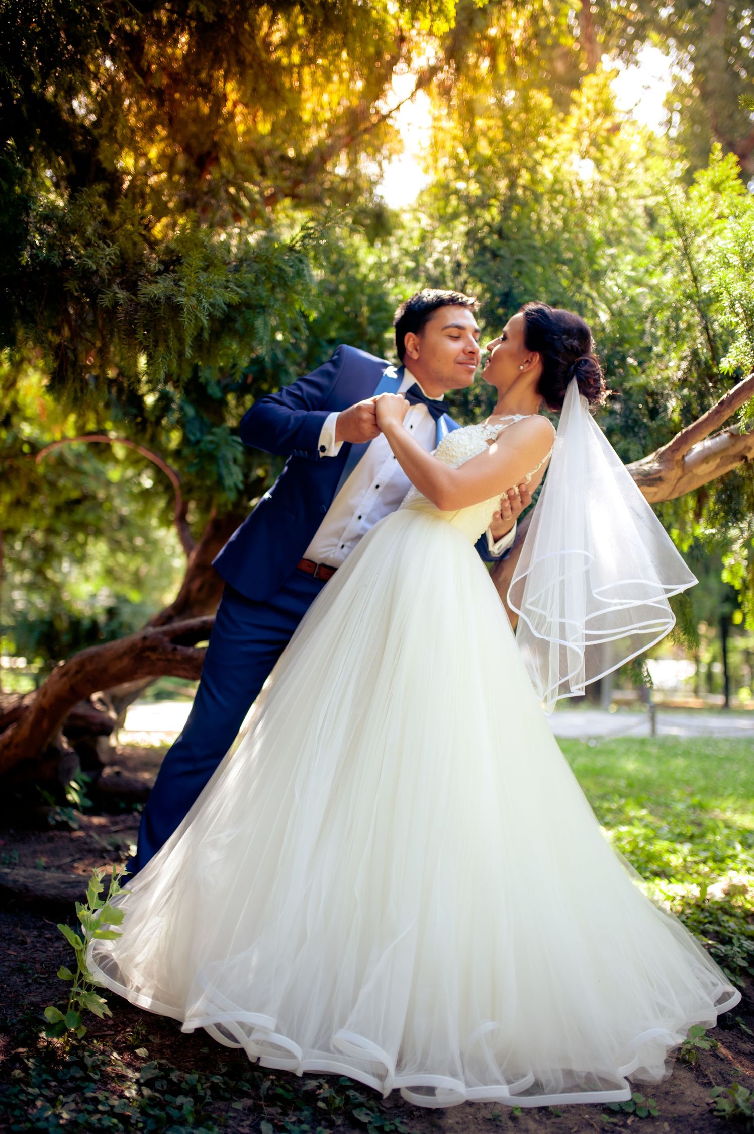 Couple in wedding attire share romantic moment under golden sunlit trees.