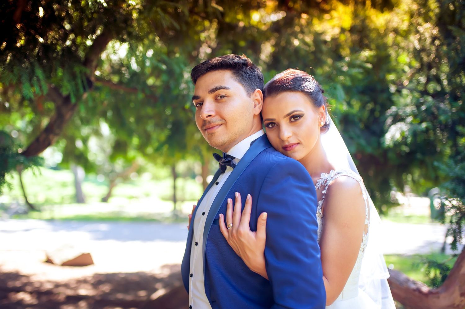 Bride in white gown and groom in blue suit pose together in a garden setting.