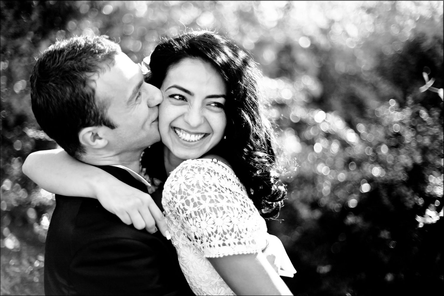 Black and white portrait of newlyweds sharing a joyful moment in garden setting.