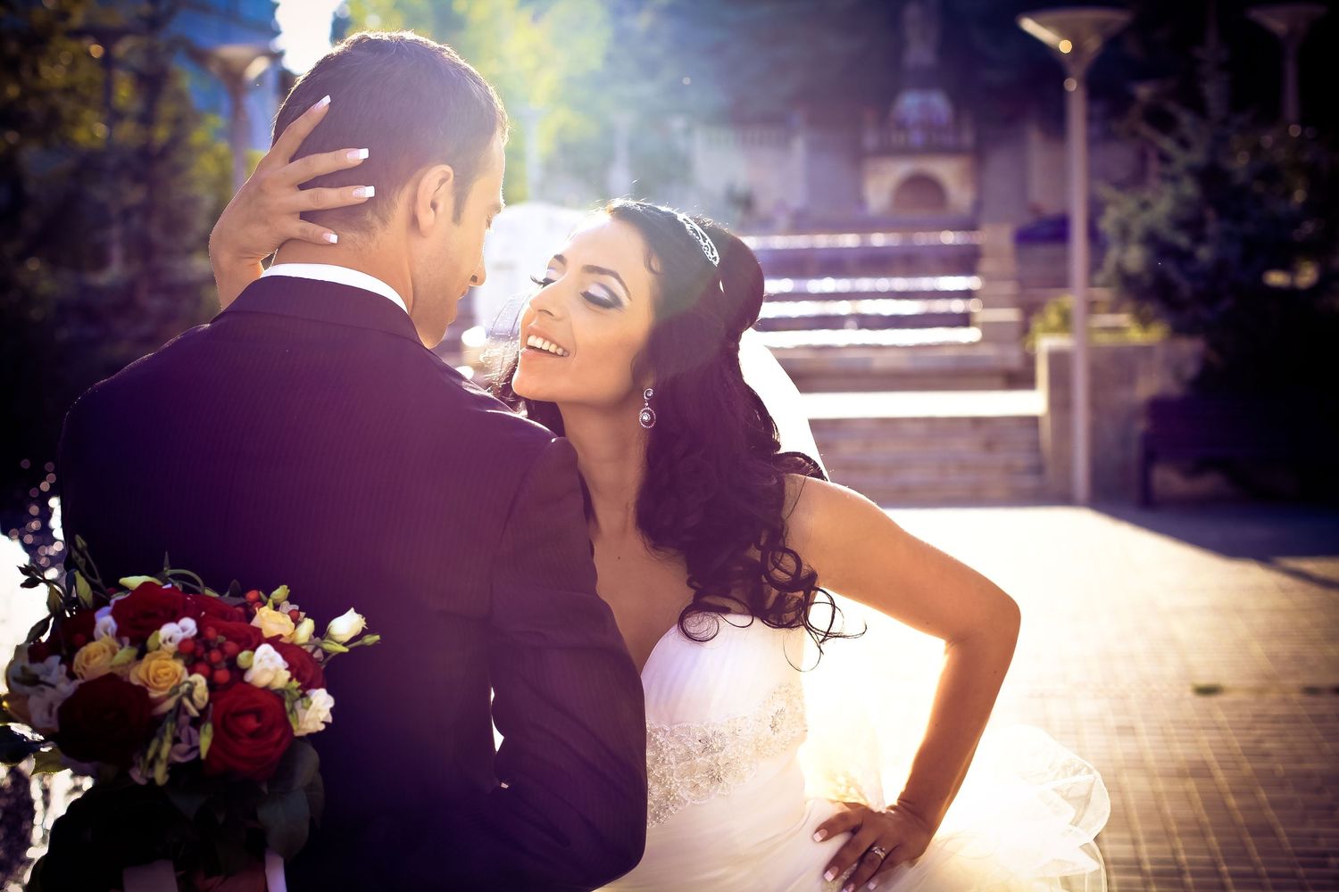Romantic sunlit wedding portrait of couple embracing outdoors with floral bouquet.