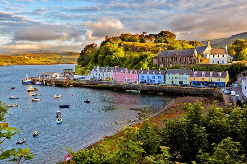 Colorful row of houses along the harbor in Portree, Isle of Skye, Scotland with boats dotting the tranquil waters at sunset.
