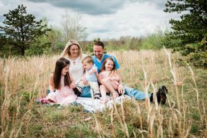 Family lying on blanket in field with cloudy sky overhead.