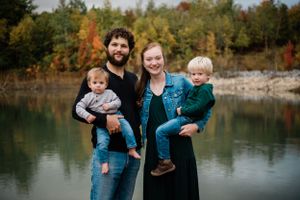 A family of four poses together by a scenic lake surrounded by fall foliage.